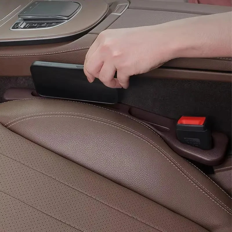 Hand placing a phone into the brown gap filler beside the seatbelt buckle in a leather car interior